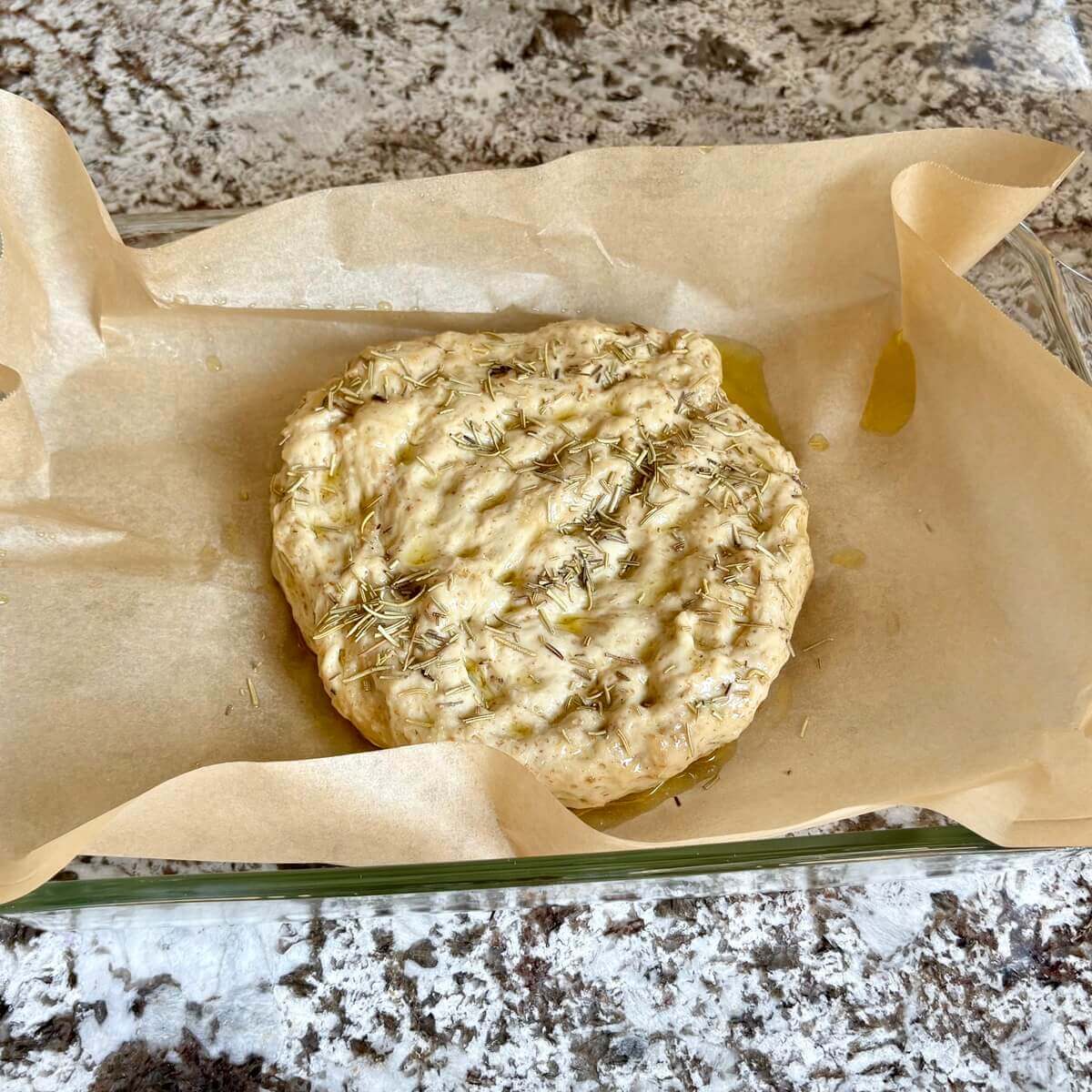 Seitan focaccia bread dough in a baking dish lined with parchment paper.