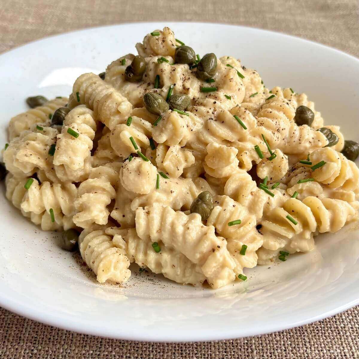 A bowl of tempeh pasta garnished with capers and chives.