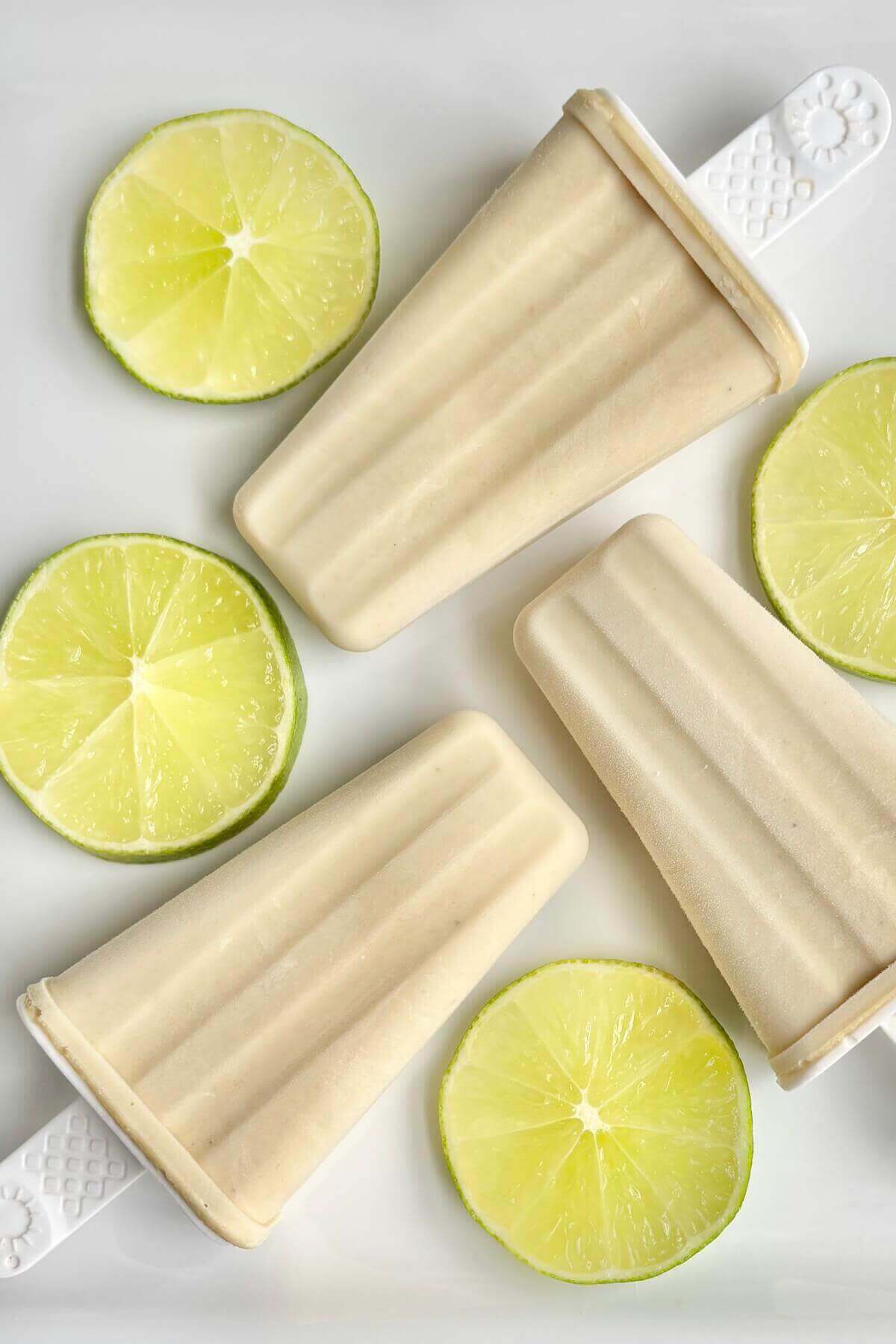 Cashew popsicles and lime slices on a white plate.