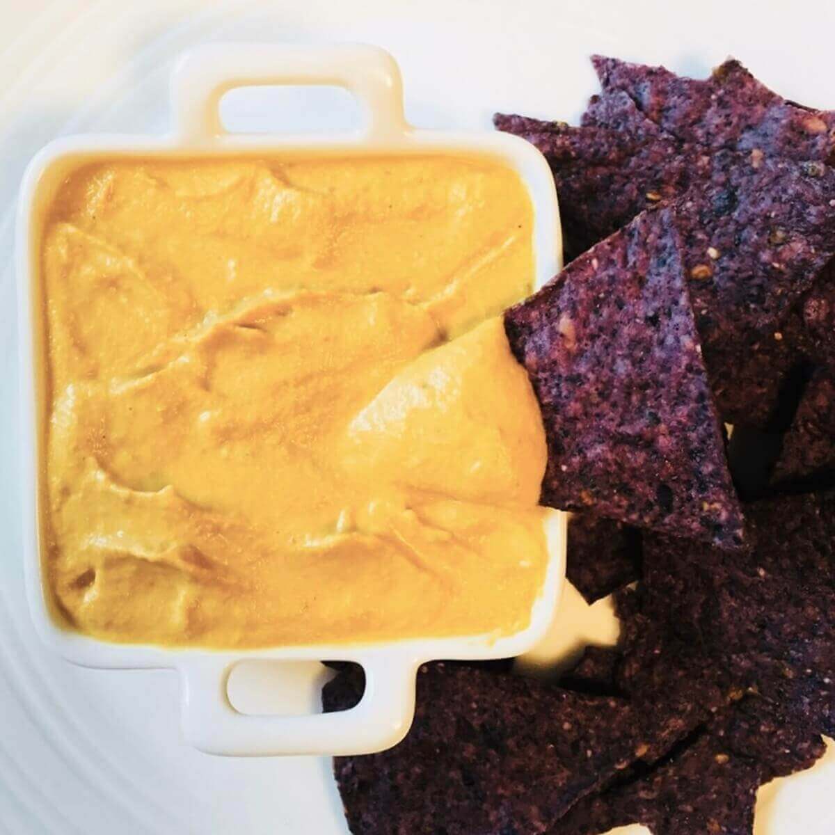 Vegan nacho cheese sauce and blue corn tortilla chips on a white plate.