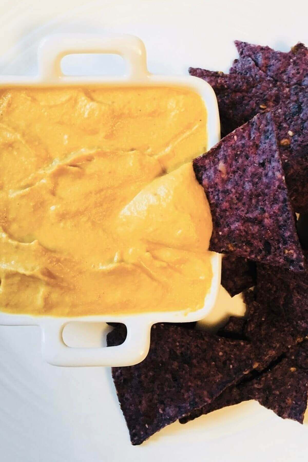 Vegan pumpkin cheese sauce next to a pile of tortilla chips.