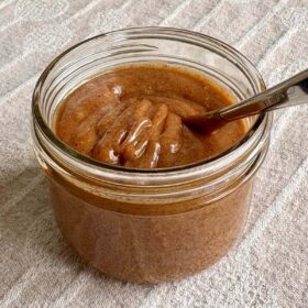 Almond butter caramel sauce in a jar with a spoon.