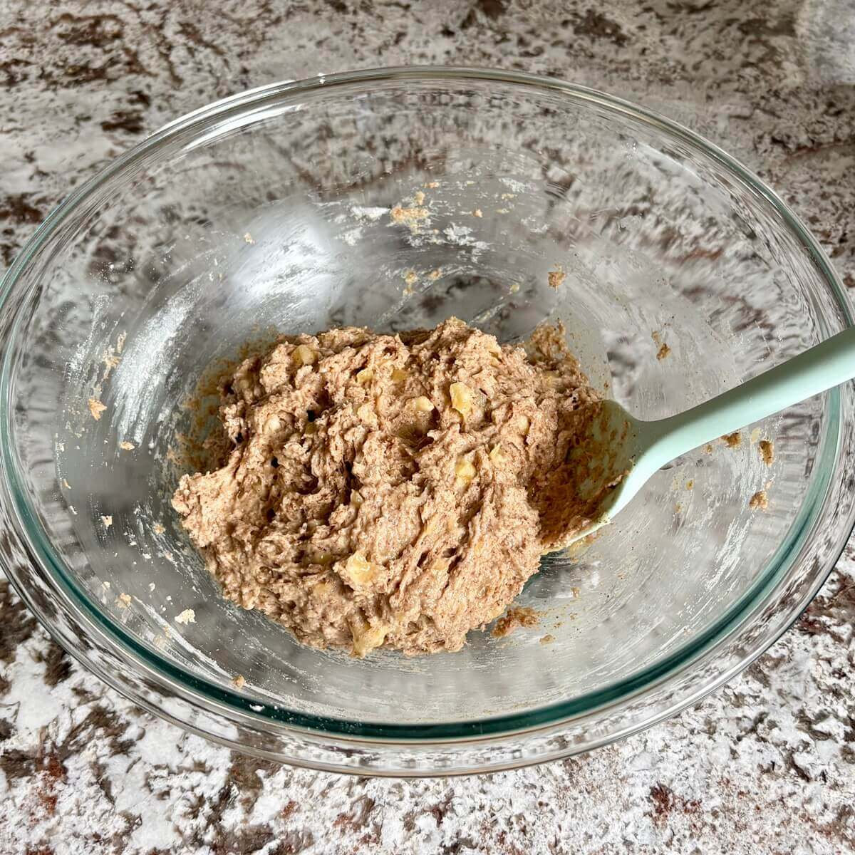 Thick banana bread batter in a glass mixing bowl.