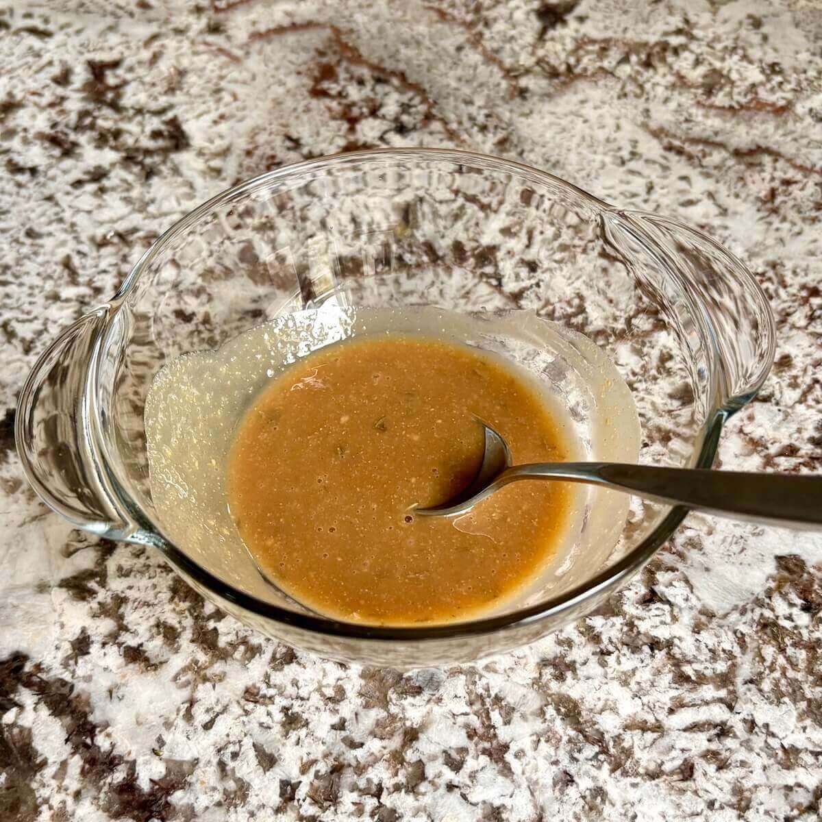 Maple mustard marinade in a glass bowl with a spoon.