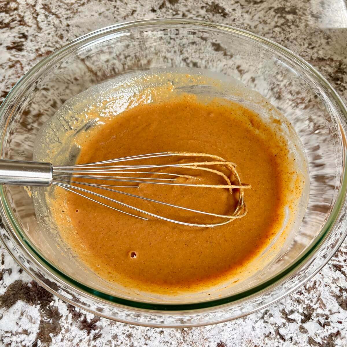 Vegan pumpkin muffin wet ingredients in a glass mixing bowl with a whisk.