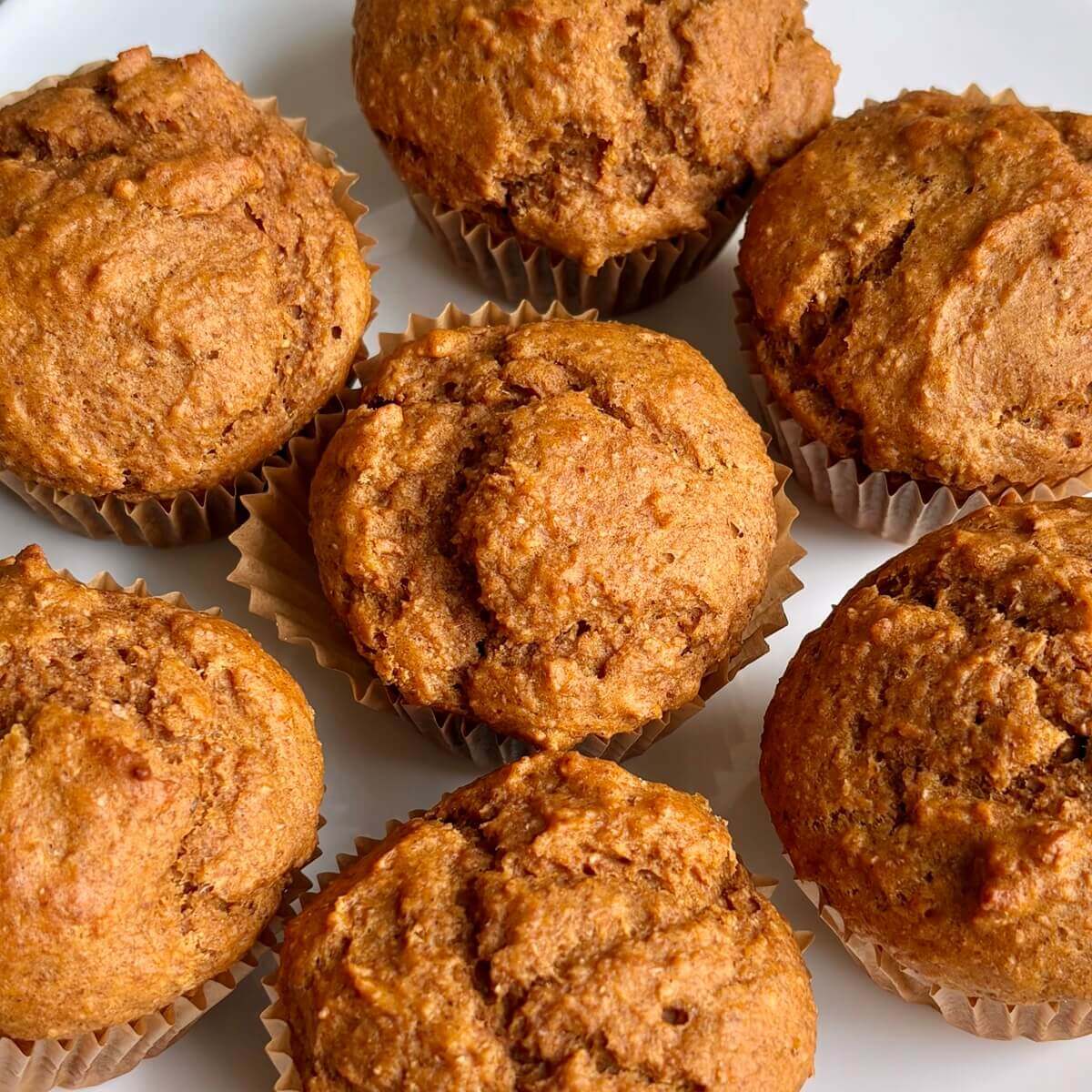 Seven vegan pumpkin spice muffins on a white plate.