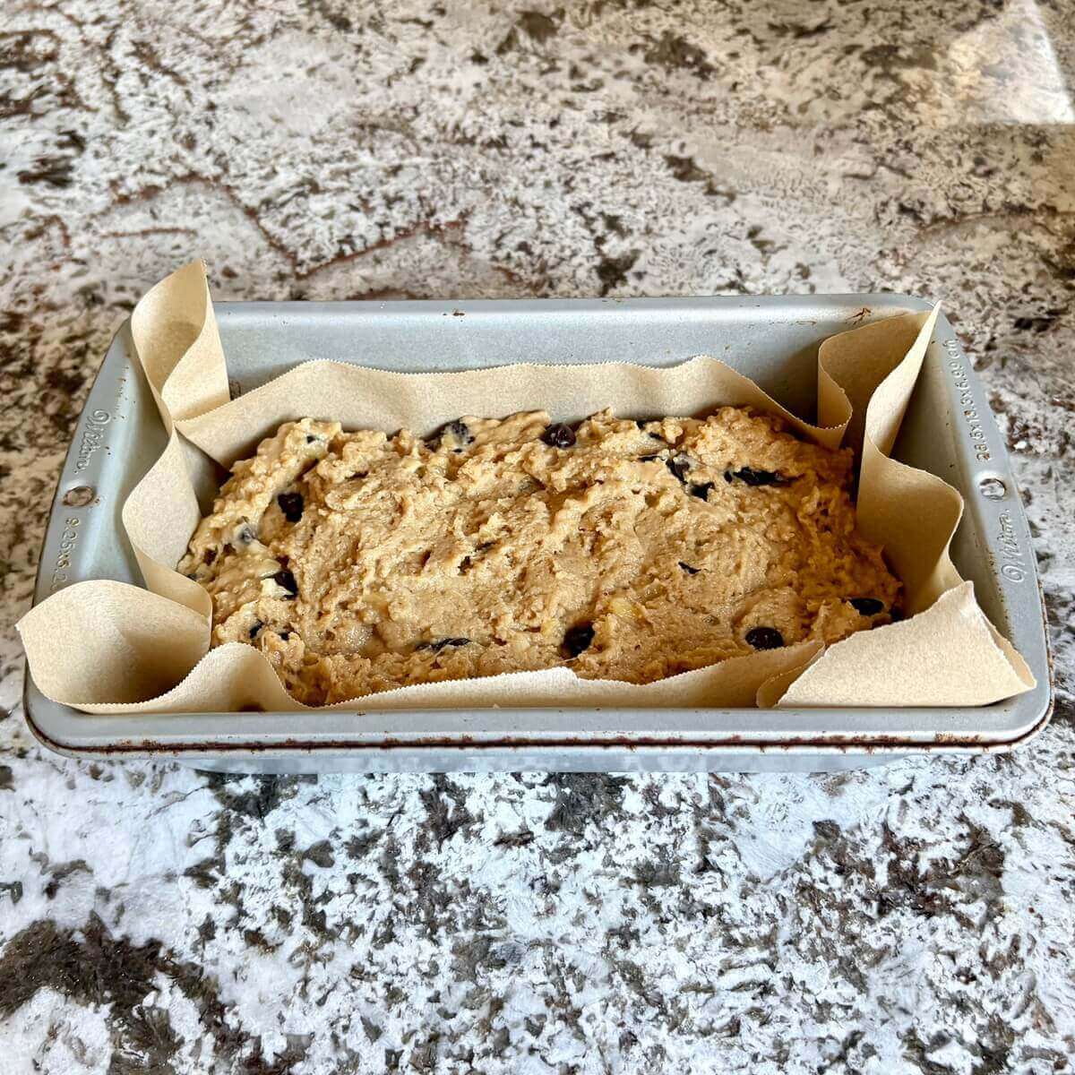 Banana bread batter in a loaf pan lined with parchment paper.