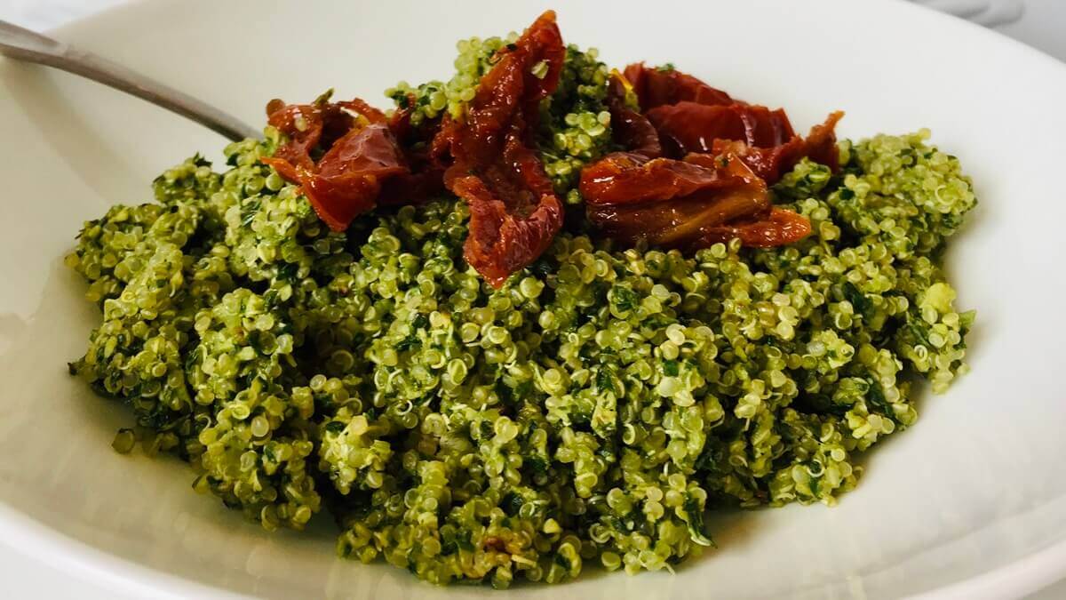 Quinoa tossed with pesto sauce with sun-dried tomatoes on top.