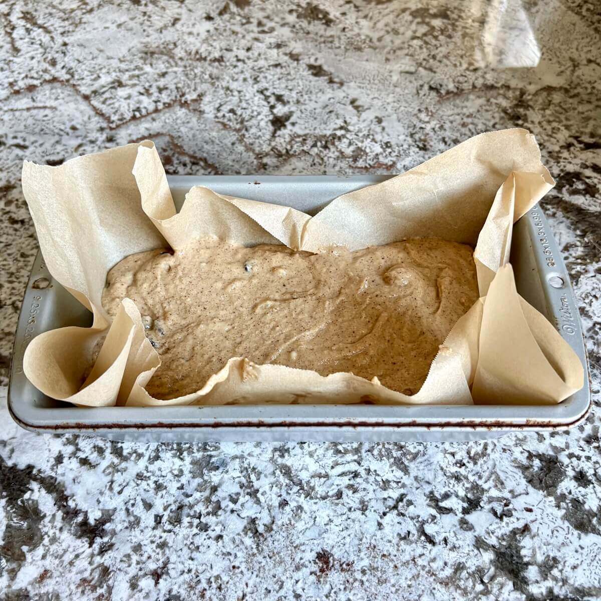 Banana bread batter in a loaf pan lined with parchment paper.