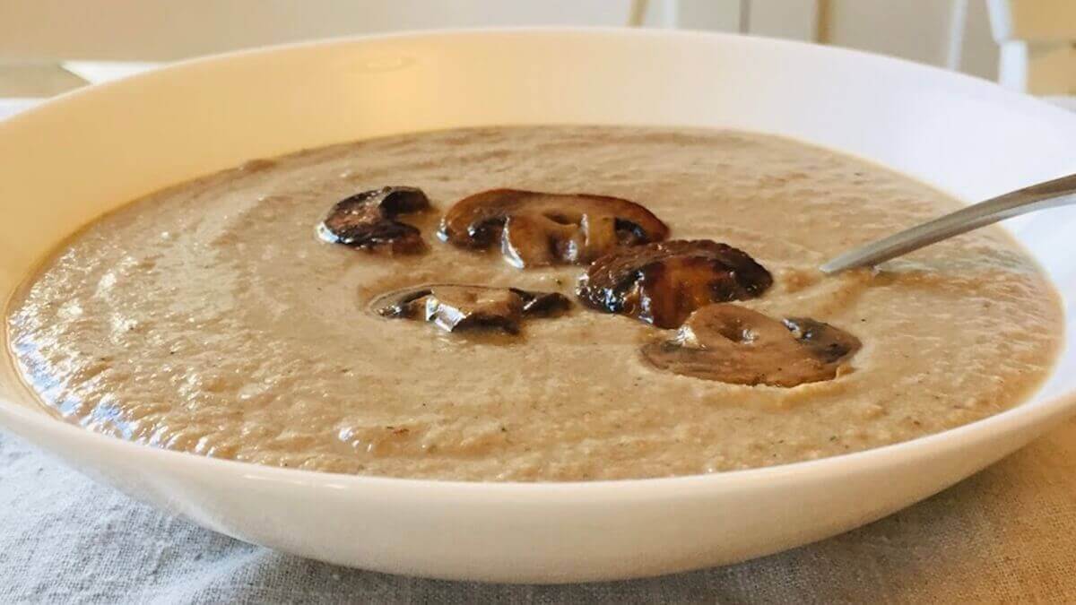 A bowl of vegan mushroom pureed soup with sliced cooked mushrooms on top.