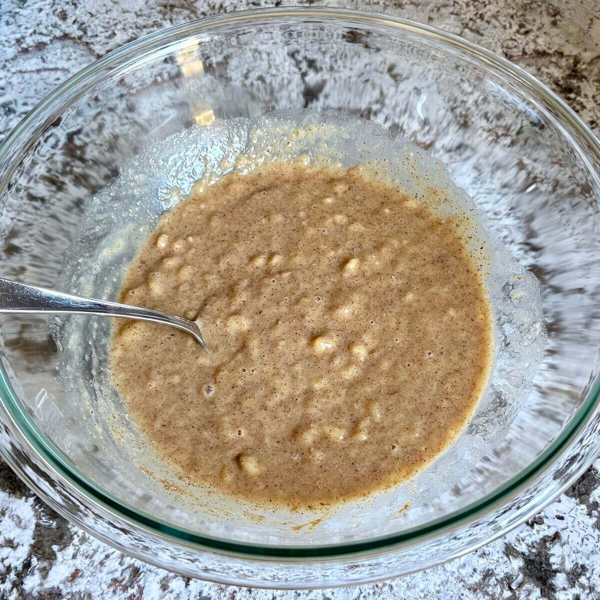 Wet ingredients for banana bread in a bowl with a spoon.